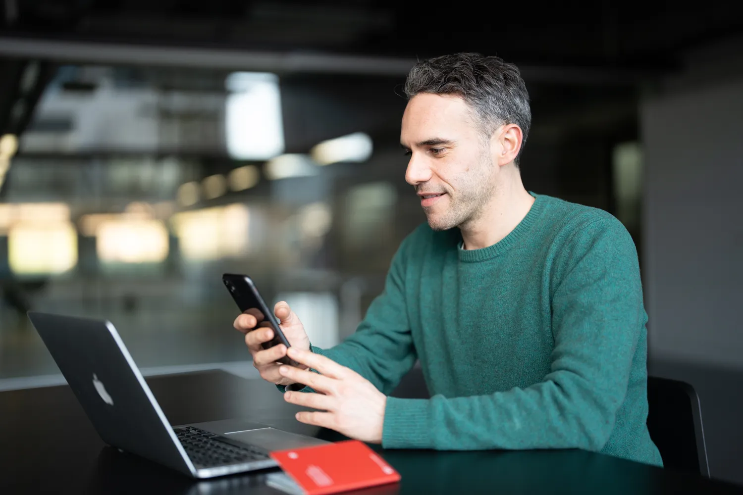 Ein Mann sitzt an einem Laptop, er ist am Smartphone beschäftigt. Nebem ihm liegt ein Schweizer Reisepass.